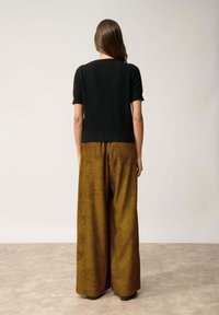 Svart kortärmad tröja kombinerad med hög midja, vida cordurobyxor i en varm brunt med vertikala ränder. Slät textur.