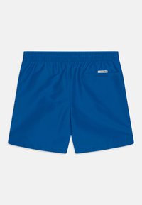 Pantaloni da bagno blu realizzati in tessuto leggero, con vita elasticizzata, una tasca posteriore e un piccolo etichetta con logo sul lato.