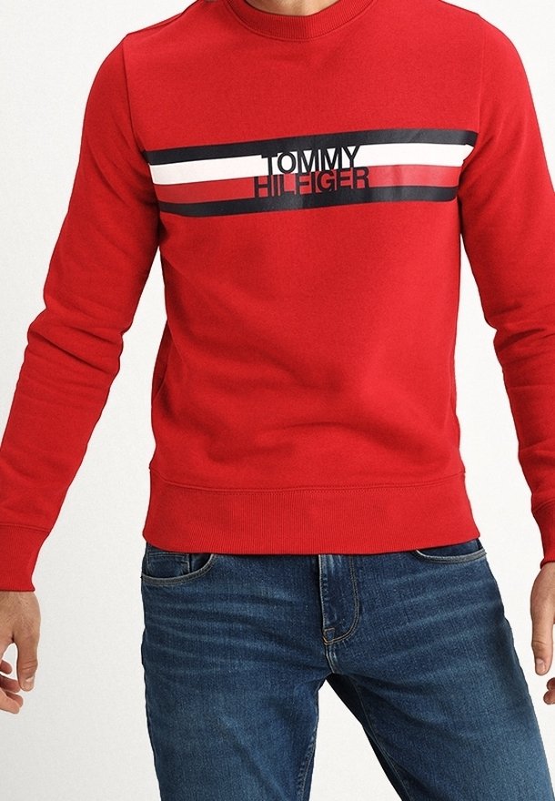 Sweat-shirt rouge à manches longues avec des rayures horizontales noires, blanches et rouges et le texte "Tommy Hilfiger", porté avec un jean en denim bleu.