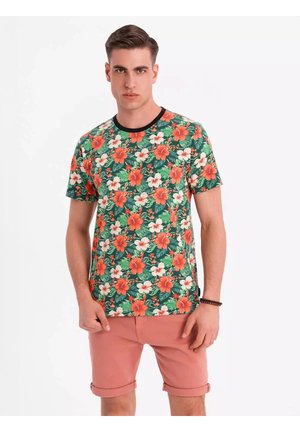 Krátký rukáv zeleného trička s květinovým vzorem červeného a bílého hibiskusu, černý límec, v kombinaci se světle růžovými šortkami.