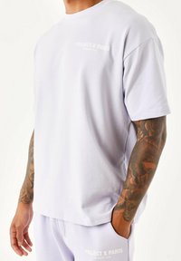 Camiseta lila hecha de una tela suave, con cuello redondo y mangas cortas. En la parte frontal está impreso en blanco "PROJECT X PARIS MEMBERS' CLUB".