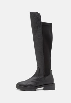 Bottes noires montantes en cuir texturé avec un pied en cuir et un tige en tissu noir lisse, équipées d'une semelle en caoutchouc épaisse et de quincaillerie minimale.