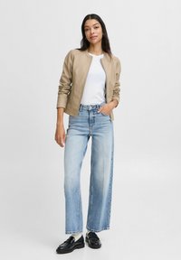 Chaqueta bomber de cuero beige con cuello acanalado, camiseta blanca, jeans de tiro alto de mezclilla azul claro y zapatos de charol negros.