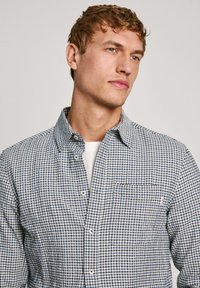 Camisa de cuadros en azul y blanco, hecha de algodón. Presenta un cuello tipo button-down y un bolsillo en el pecho. Textura suave con un corte clásico.