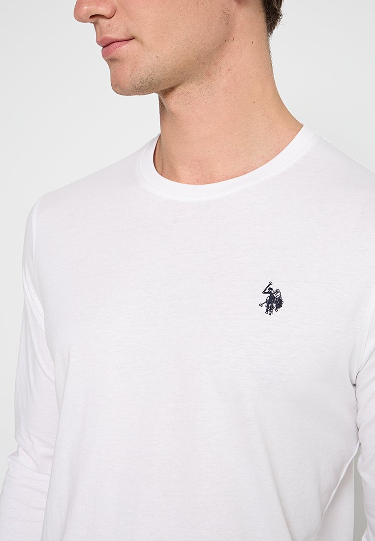 T-shirt bianco a maniche lunghe realizzato in tessuto leggero, con un piccolo logo ricamato nero sulla parte superiore sinistra del petto. Collo rotondo.