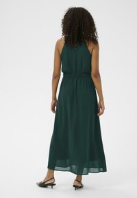 Rochie lungă, de culoare verde închis, dintr-un material ușor, cu o ușoară volanță la tiv și o talie elastică. Textură netedă și design simplu.