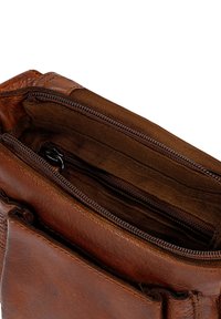 Interieur van een bruine leren tas met een ritscompartiment en twee kleinere zakken, met een gladde textuur en duurzame stiksels.