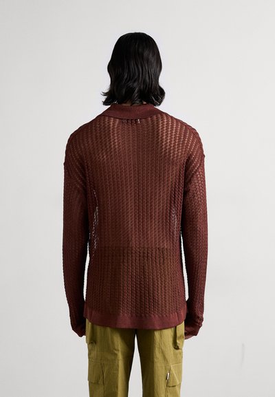 Maglione lungo a maniche lunghe in maglia rossa con un motivo testurizzato, dotato di colletto e design con schiena scoperta. Abbinato a pantaloni cargo verde oliva.
