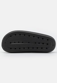 Black rubber shoe sole with a zigzag tread pattern and multiple perforations for breathability. Flat, rounded toe design.