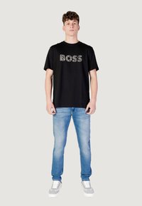 Zwarte katoen t-shirt met het "BOSS" logo op de voorkant, gecombineerd met lichtblauwe denim jeans en grijze sneakers. Eenvoudig casual ontwerp.