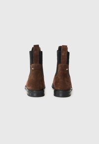 Bottines en daim marron avec des panneaux latéraux en élastique, une semelle en caoutchouc noir robuste et un petit logo accentué à l'arrière du talon.