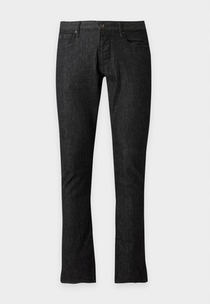 Homme portant des lunettes de soleil foncées, un polo bleu marine à manches courtes avec fermeture éclair, un pantalon gris foncé et des chaussures habillées noires, debout sur un fond blanc.