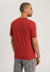 T-shirt rosso a maniche corte in cotone morbido, con scollatura a girocollo classica. Indossato con pantaloni del pigiama a fantasia, che mostrano motivi floreali in grigio e blu.