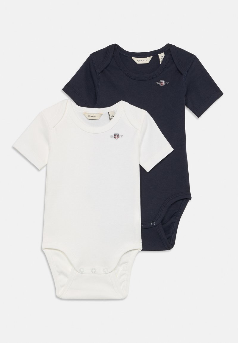 Deux bodies pour bébé : un blanc et un bleu marine. Les deux ont des manches courtes, des cols ronds et des boutons-pression à la base. Logo GANT brodé.