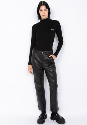 Haut à col roulé noir côtelé associé à un pantalon en cuir noir taille haute. Les chaussures sont épaisses et noires avec une semelle large.