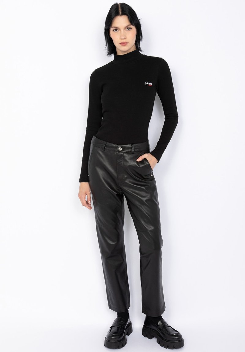 Haut à col roulé noir côtelé associé à un pantalon en cuir noir taille haute. Les chaussures sont épaisses et noires avec une semelle large.