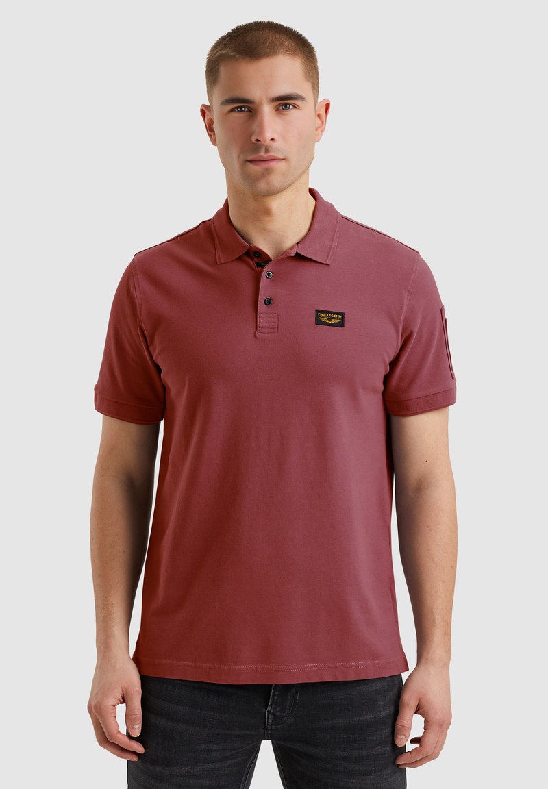 Rdeča polo majica iz bombaža, s kratkimi rokavi, sprednjim zapenjanjem na tri gumbke in majhnim logotipom na levem prsnem delu.