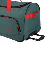 Borsa da viaggio verde con accenti rossi, dotata di manico retrattile, bordi neri e scomparti con zip per riporre oggetti.
