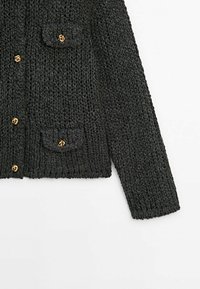 Cardigan en maille épaisse gris foncé avec manches longues, deux poches à rabat et boutons dorés en forme de nœud sur fond blanc.