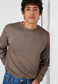 Bruine lange mouwen shirt van gladde stof, met een ronde hals en een losse pasvorm, gecombineerd met blauwe denim jeans.