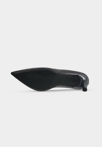 Escarpin en cuir verni noir à bout pointu montré de la semelle avec un talon bas effilé sur fond blanc.