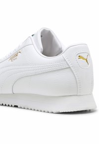Puma Roma sneakers, fehér bőr felsőrész, lekerekített orr, texturált felület, arany logó részlet, lapos gumi talp enyhe mintázattal.