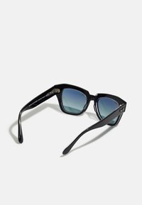 Ochelari de soare negri cu design geometric, lentile graduat de culoare albastră și finisaj lucios. Prezintă accente metalice pe braț și brațe curbate.