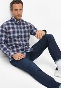 Blau-rot kariertes Flanellhemd mit Knopfverschluss, kombiniert mit dunkelblauen Jeans und weißen Sneakers, zeigt einen lässigen Schnitt und modernes Design.