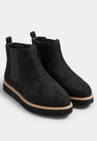 Czarne zamszowe botki za kostkę z elastycznymi panelami bocznymi, okrągłym noskiem i kontrastującą jasnobrązową podeszwą z białym szwem. Posiadają zamek błyskawiczny z boku.