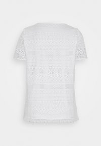 Vit spets blus med kort ärm och ett texturerat mönster med horisontella rader av cirklar och diamanter, vågig nederkant och rund halsringning.