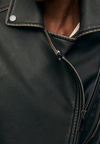 Černá kožená bunda s ostrým límcem, stříbrným knoflíkem a bočním zipem. Materiál má texturovaný povrch s viditelným šitím.