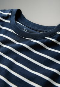 Camiseta de algodón azul marino con rayas blancas horizontales, que presenta un cuello redondo y una textura suave. Etiqueta en la zona del cuello.