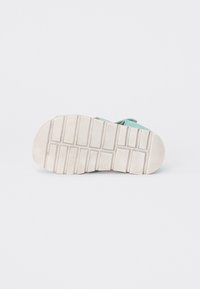 Sandalsula i lätt beige gummi med djupa mönster för grepp. Överdelen är i ljusblått tyg med justerbara remmar och mjuk textur för komfort.
