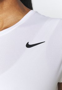 Camiseta deportiva blanca de Nike con escote en V, que presenta un logo negro en el pecho izquierdo y un tejido de malla texturizada para mayor transpirabilidad.