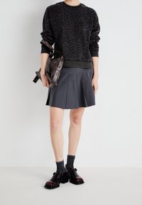 Czarna bluza w panterkę, szara spódnica plisowana, ciemne skarpetki i błyszczące czarne buty. Brązowa torba na pasku. Prosty i funkcjonalny design.