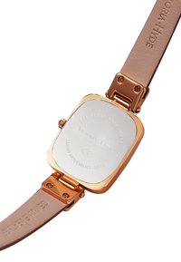 Montre avec un boîtier carré en acier inoxydable aux accents en or rose, bracelet en cuir crème, et détails de marque et de mouvement gravés au dos.