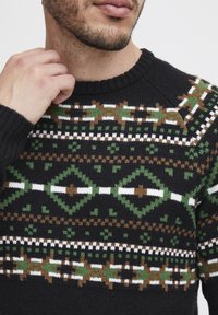 Pulover negru tricotat cu un model geometric în verde, maro și alb. Gât la bază cu margine ondulată și manșete ribbate, confecționat dintr-un material texturat.