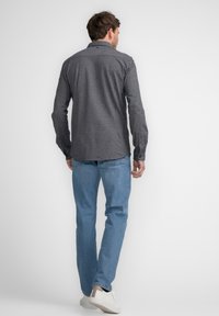 Mørk button-down skjorte med et struktureret mønster, parret med lyseblå jeans og hvide sneakers. Skjorten har en spids krave og lange ærmer.