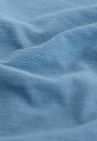 Lichtblauwe stof met een gladde textuur, gekenmerkt door zachte golven en een subtiel, fijn geweven patroon. Geen zichtbare patronen of hardware.