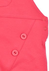 Roze katoenen kledingstuk met een gladde textuur, met twee bijpassende knopen en een diagonale naad nabij het zakgebied.