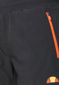 Svarta shorts med elastisk midja, med en orange dragkedjeficka och en logotyp med gula, röda och svarta accenter. Mjuk textur.