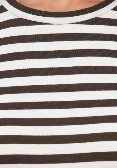 Κοντινό πλάνο ενός ατόμου που φοράει μαύρο και άσπρο πουκάμισο με οριζόντιες ρίγες και στρογγυλή λαιμόκοψη.