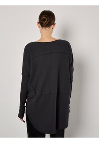 Maglietta nera a maniche lunghe con parte superiore texturizzata e a costine e parte inferiore liscia. L'orlo arrotondato contrasta con il design dritto.