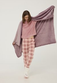 Piumino viola morbido e vellutato e top rosa abbinati a pantaloni da pigiama a scacchi. Pantofole bianche e soffici completano il look accogliente.