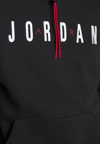 Felpa nera con cappuccio caratterizzata da audace scritta "JORDAN" in bianco e rosso, tasca frontale e dettagli in rosso nei lacci. Texture del tessuto liscia.