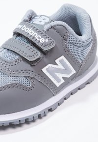 Szare buty sportowe z materiału z siatki i skóry, z rzepem, białymi akcentami i wzorzystą gumową podeszwą.