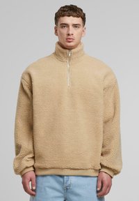Pull en polaire beige avec col haut et demi-zip. Surface texturée avec une coupe décontractée et des poignets et un ourlet côtelés. Design décontracté.
