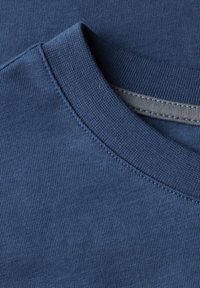 Modré bavlněné tričko s kulatým výstřihem, ribovaným límcem a jemným švem. Tkanina je hladká s jemnou strukturou.