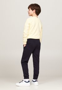 Maglione giallo chiaro con scollo rotondo indossato con pantaloni jogger blu navy. Sneakers bianche con dettagli blu navy. Tessuto morbido; vestibilità casual.