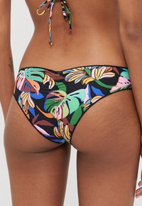 Reversible bikini bottom in vibrant floral print on black background, featuring a smooth texture, low rise, and minimal coverage design.